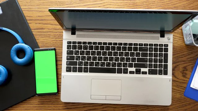 Smartphone with green screen next to a laptop on a business table. Above top view dolly footage