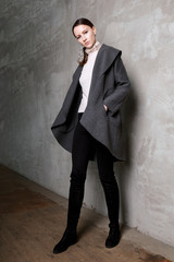 high fashion portrait of young elegant woman in studio on greyconcrete vintage wall. Grey coat