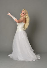 full length portrait of blonde girl wearing white corset gown. standing pose on grey studio background.