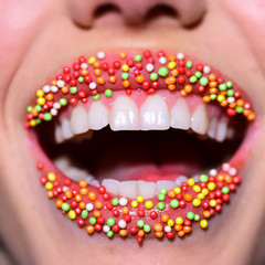 Smile lips. Multicolored delicious mouth. Beautiful lips with small sweets. Dessert and sexy taste. White teeth in female mouth. Beautiful smile close-up. Candy and confectionery. Lipstick cosmetics