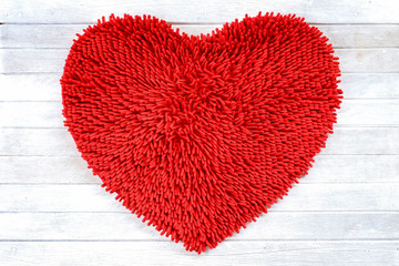 Red heart shape cleaning feet doormat or carpet texture on white wooden background.