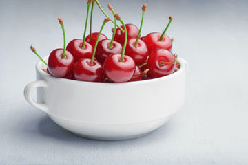 White bowl of ripe red cherry on a light wooden background