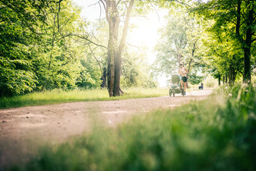 Running woman with baby stroller enjoying summer in park - 209360086