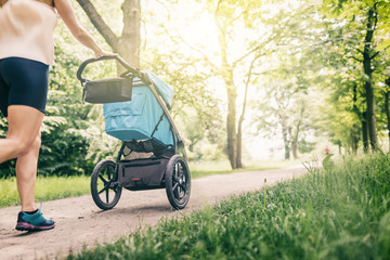 Running woman with baby stroller enjoying summer in park