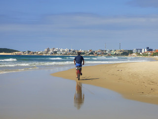 Man riding a bike at Ingleses beach, city in the background - Florianopolis, Brazil