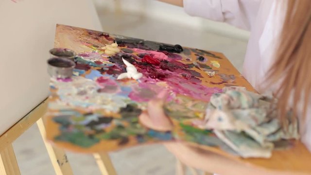 The artist mixes oil paints on a palette with a brush, close-up.