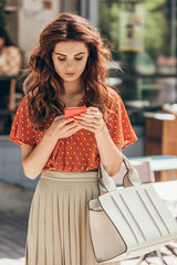 Fototapeta premium portrait of young stylish woman using smartphone on street