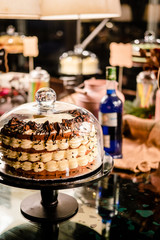 Tiramisu layer cake under glass bell dome. Cake stand, dessert buffet, storage. Food photography concept