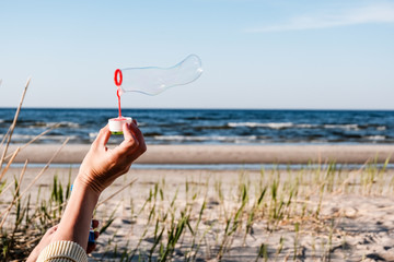 hand of young female playing with soap bubbles outdoors at beach