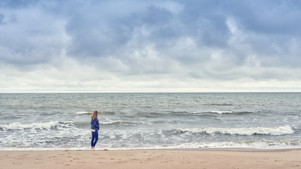 Frau steht alleine am Strand und blickt auf das Meer