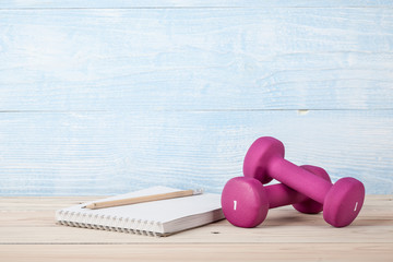 Fitness concept with pink dumbbells and notepad for workout plan