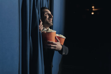 portrait of a young man walks alone into the cinema carrying two boxes of popcorn, happy and...
