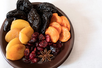 Dried fruits in a bowl. On the plate there are prunes, dried apricots, dried cranberry, dried mooseberry. A white background. View from above. Close-up. Macro photography.