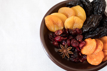 Dried fruits in a bowl. On the plate there are prunes, dried apricots, dried cranberry, dried mooseberry. A white background. View from above. Close-up. Macro photography.