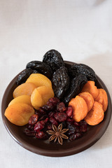 Dried fruits in a bowl. On the plate there are prunes, dried apricots, dried cranberry, dried mooseberry. A white background. View from above. Close-up. Macro photography.