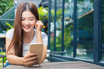 Young attractive asian woman in casual clothes sitting outdoor listening to music from her smart phone