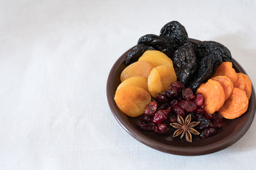 Dried fruits in a bowl. On the plate there are prunes, dried apricots, dried cranberry, dried mooseberry. A white background. View from above. Close-up. Macro photography.