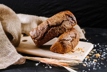 sweet and tasty bread and wheat on black wooden background