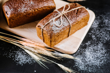sweet and tasty bread and wheat on black wooden background