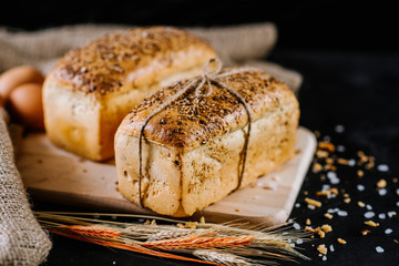 sweet and tasty bread and wheat on black wooden background