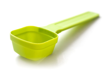closeup of green plastic dose spoon on white background