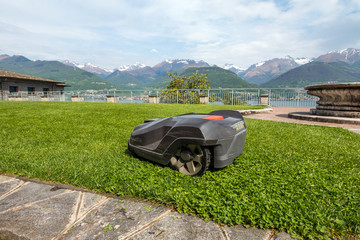 a robotic lawn mower working on a green grass field near Como lake. Italy