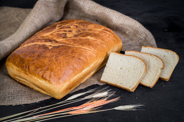 Sweet tasty bread and wheat on wooden background
