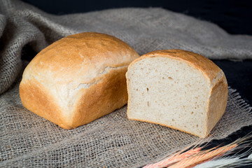 Sweet tasty bread and wheat on wooden background