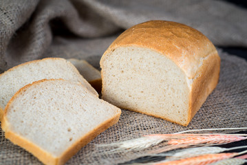 Sweet tasty bread and wheat on wooden background