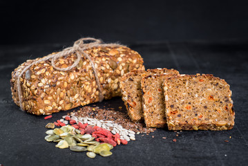 Tasty sweet rye bread with seeds on black wooden background