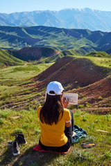 Fototapeta na wymiar A girl in the background of mountains drawing a landscape. Sits with his back. Painting outdoors. Kazakhstan. Mountain landscape