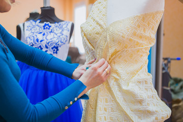 Professional tailor, designer working with new model tailoring dress on mannequin in studio, atelier. Fashion and tailoring concept