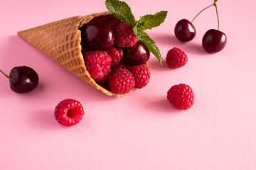 Ice cream cone  with raspberries and cherry on the pink  background