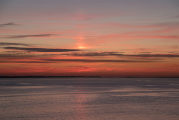 Orange sky reflected on ocean with dark thin striped cloud background