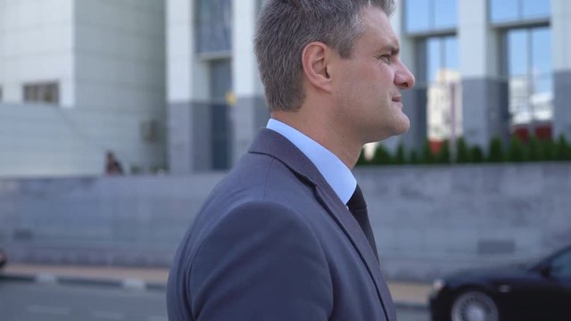 A gray-haired middle-aged man in a suit goes to a meeting on the background of a business center. Business and success. portrait to the waist. moving shot 4K