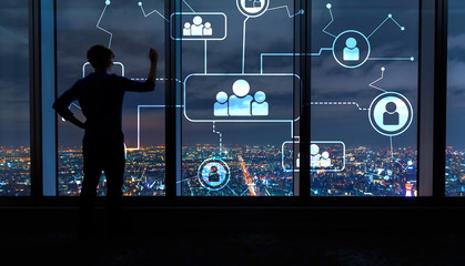 Social connections with man writing on large windows high above a sprawling city at night