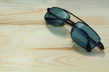 Fototapeta na wymiar Old black sunglasses lying on a new wooden board. Close-up. Background.