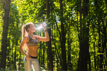Naklejka na ściany i meble Fitness beautiful woman drinking water and sweating after exercising on summer hot day in park. Female athlete after work out.