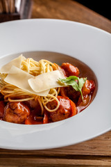 The concept of Spanish cuisine. Italian pasta, spaghetti in a white plate with a bolognese and meatballs on a wooden table in a restaurant.