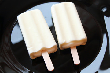 Creamy ice cream on a stick in white glaze on a black plate. Eskimo. Close-up. Background.