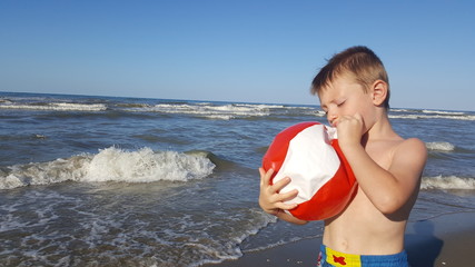 bambino in riva al mare gonfia un pallone da spiaggia