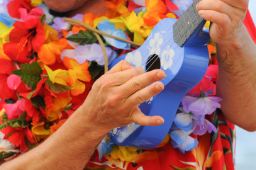 A man playing a Hawaiian ukulele wearing a bright flowered shirt