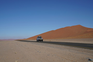 Travellers in vehicle travelling raod through Sossusvlei dune area in Namibia.