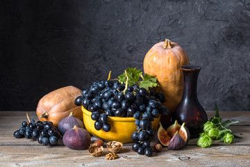 autumn still life, pumpkin, grapes, figs and nuts on a wooden table, dark background