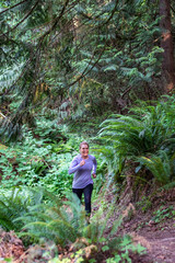 Naklejka na ściany i meble Female baby boomer in a purple top and black running pants on an evening run on a forest trail 