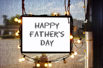 Happy Fathers Day written on hanging sign surrounded by party lights in shop window with...