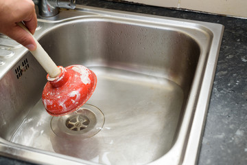 Man using a plunger with one hand and  water in sink, used to clean a clogged / blocked kitchen sink