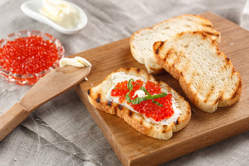 toasts with butter and Red caviar on a wooden cutting Board