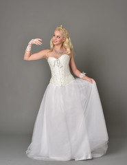 Fototapeta premium full length portrait of blonde girl wearing white corset gown. standing pose on grey studio background.