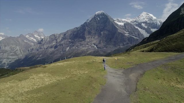 Pan-down of Mannlichen, Grindelwald, Canton of Berne. Shot captures people walking on mountain passes and snowy summits of Eiger, Monch and Jungfrau the background.